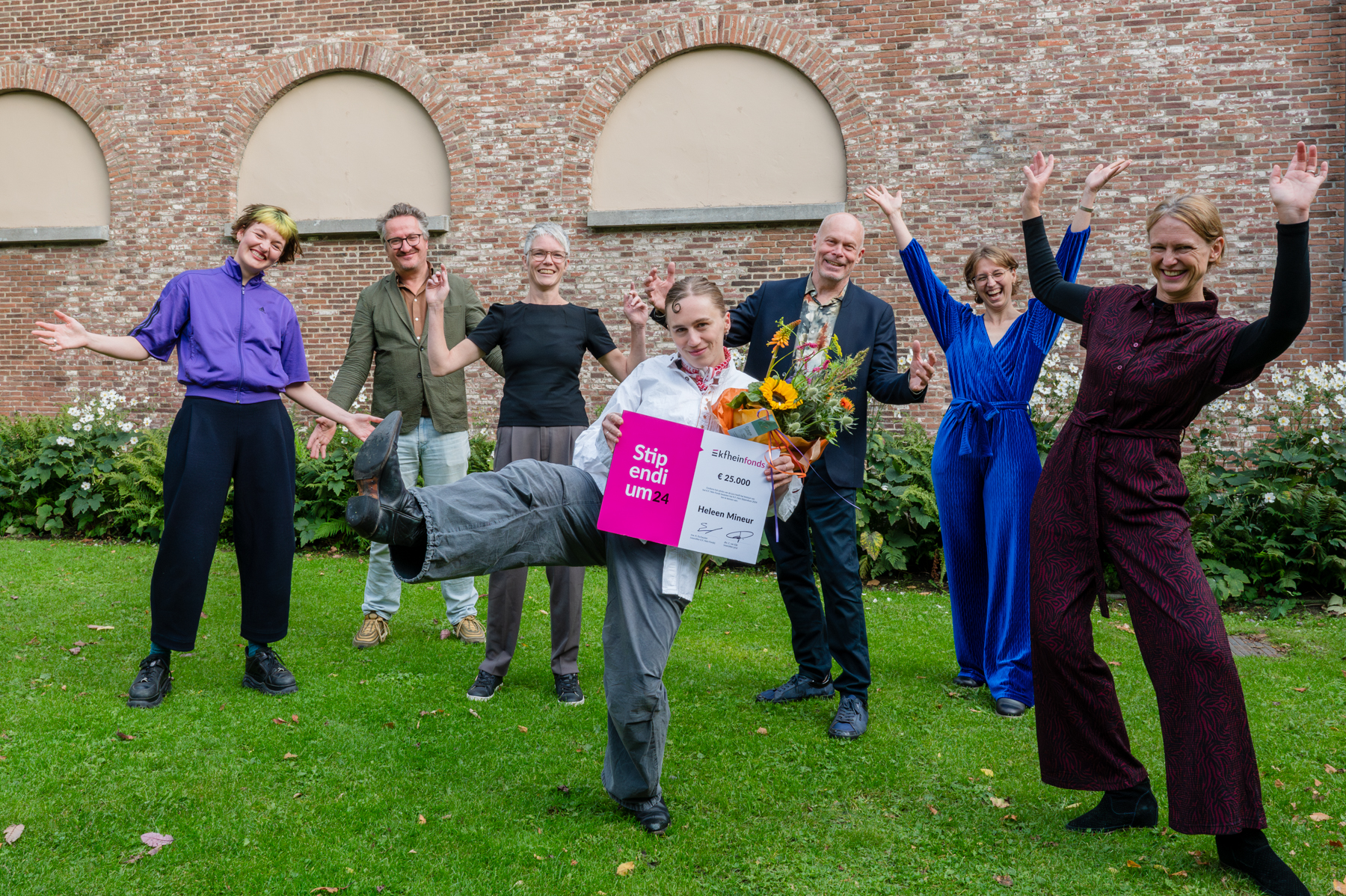 Heleen Mineur poseert temidden van juichende juryleden met haar cheque en boeket bloemen in de tuin